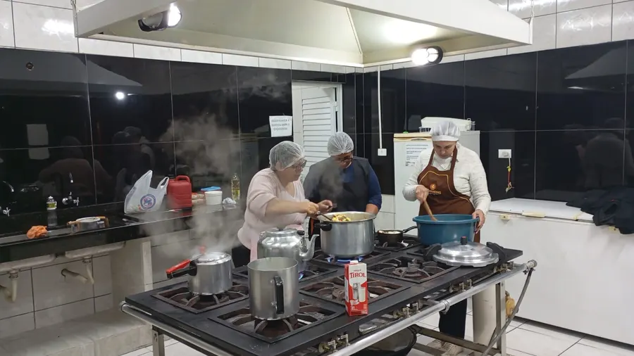 Voluntárias preparando a comida em panelas grandes no fogão industrial