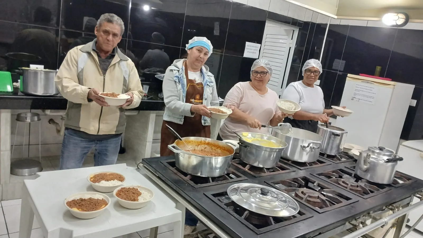Voluntários servindo pratos de comida recém-preparada na cozinha da paróquia